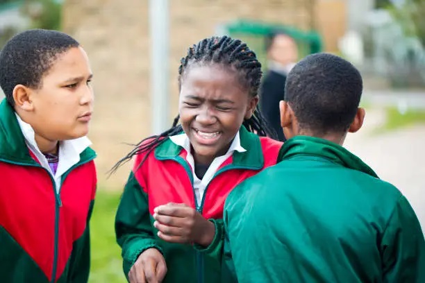 Three Nigerian secondary schoolgirls in uniform laughing and playing together outdoors.