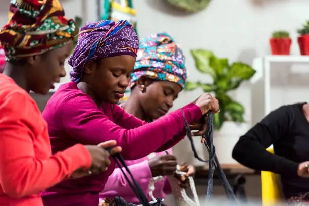 African women in colorful headwraps participating in a hands-on skill acquisition workshop.